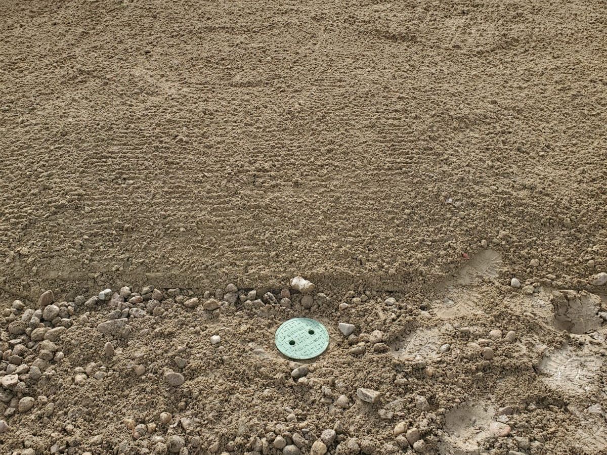 Two green sewer cleanout caps set flush at grade after backfill