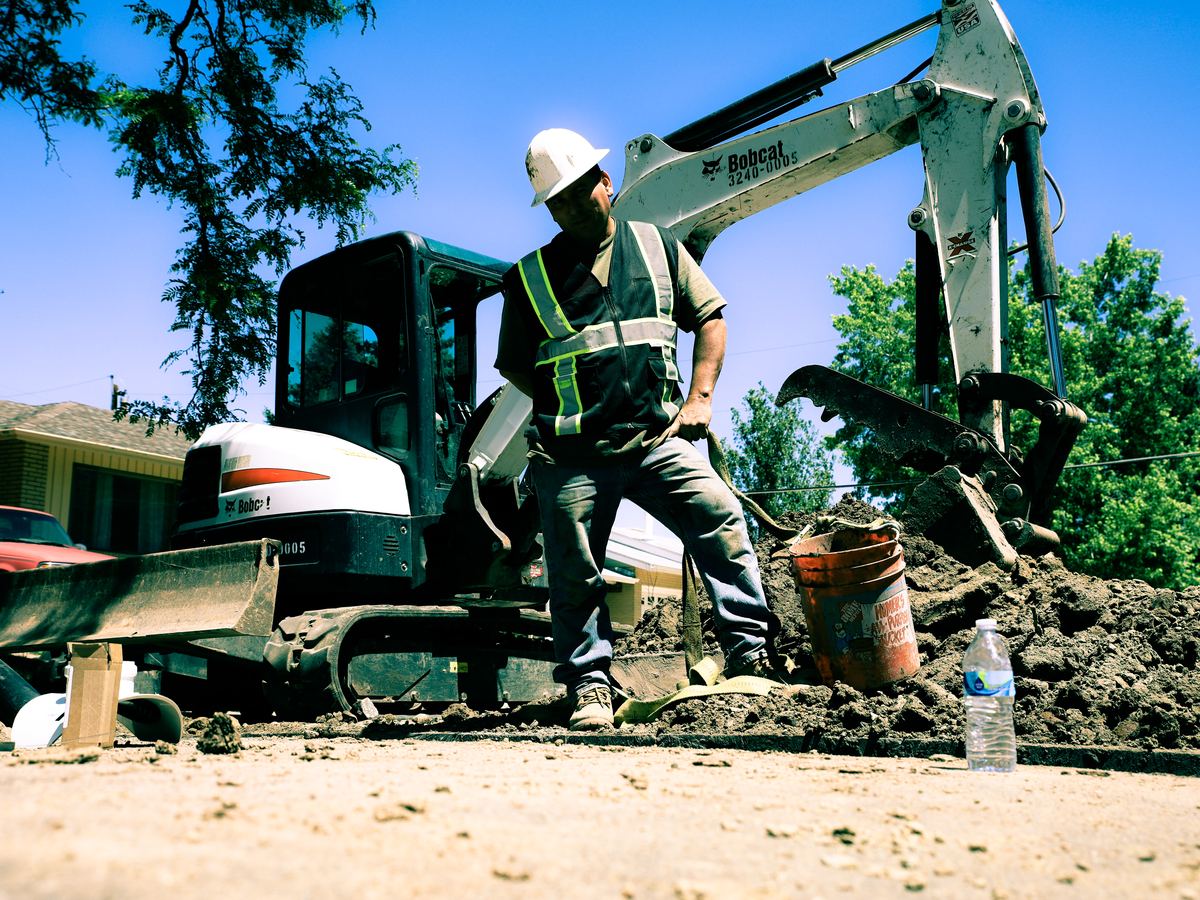 Sewer Experts operator standing beside a Bobcat excavator on a Denver sewer line job