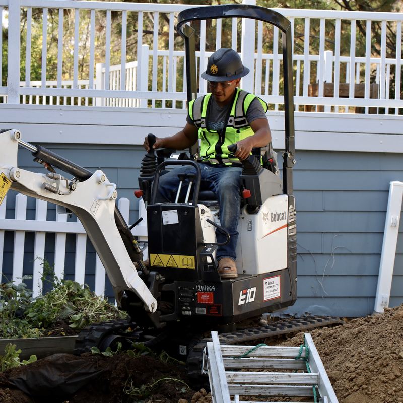 Compact mini excavator working beside a house