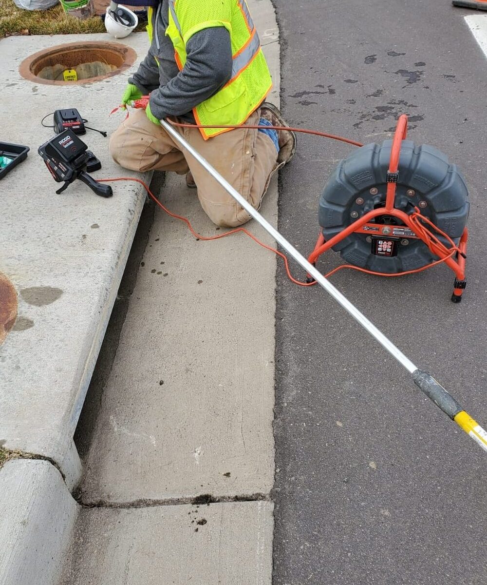 Sewer Experts technician running a locating camera into a sewer line from a curbside cleanout in Denver