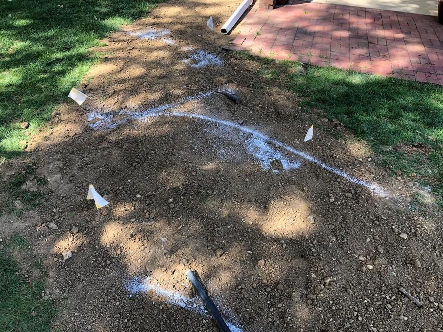 White paint marks and flags in a yard showing the path of a buried pipe