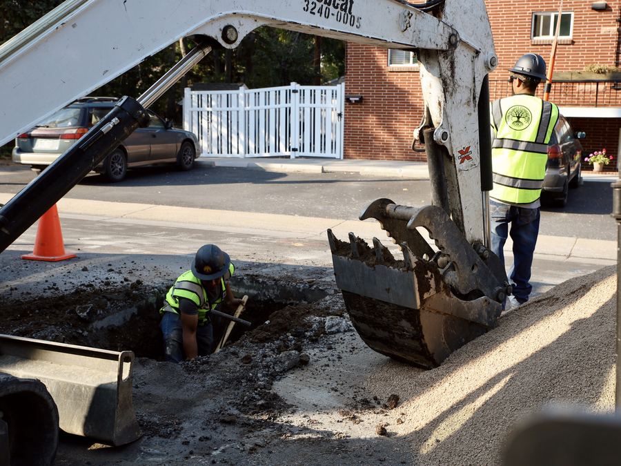 Excavator opening a trench for storm drain pipe with a crew member below